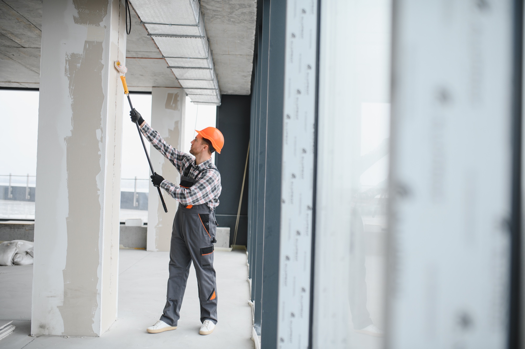 Construction worker painting walls with roller in building renovation